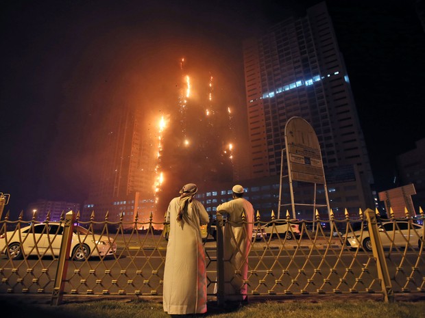 Dois homens observam incêndio nas torres residenciais no emirado de Ajman, nos Emirados Árabes Unidos, na segunda (28) (Foto: AP Photo/Kamran Jebreili)