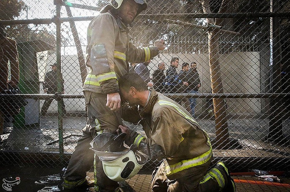 Bombeiros choram após o desmoronamento de um prédio em chamas em Teerã, no Irã. Informações iniciais apontavam que diversos bombeiros ainda estavam no interior do edifício no momento em que ele desabou (Foto: Reuters/Tasnim News Agency)